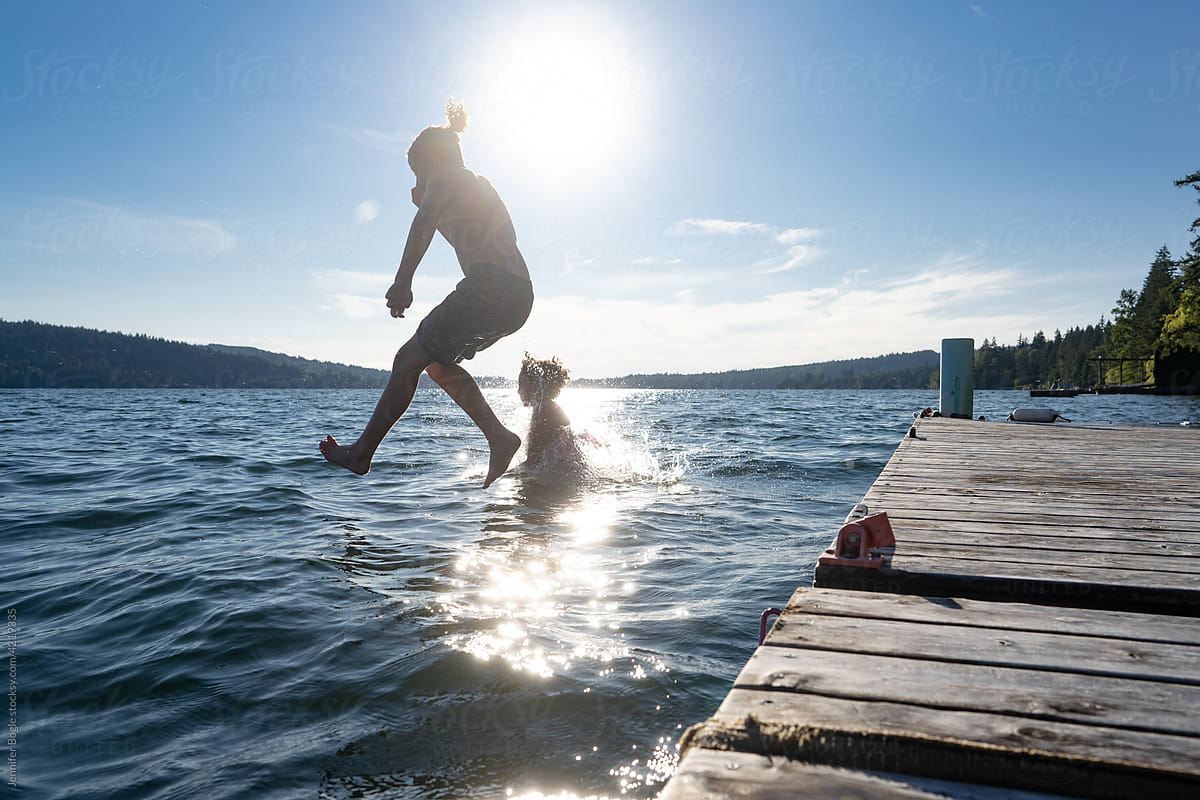 Silhouetted Siblings jump into lake from dock
