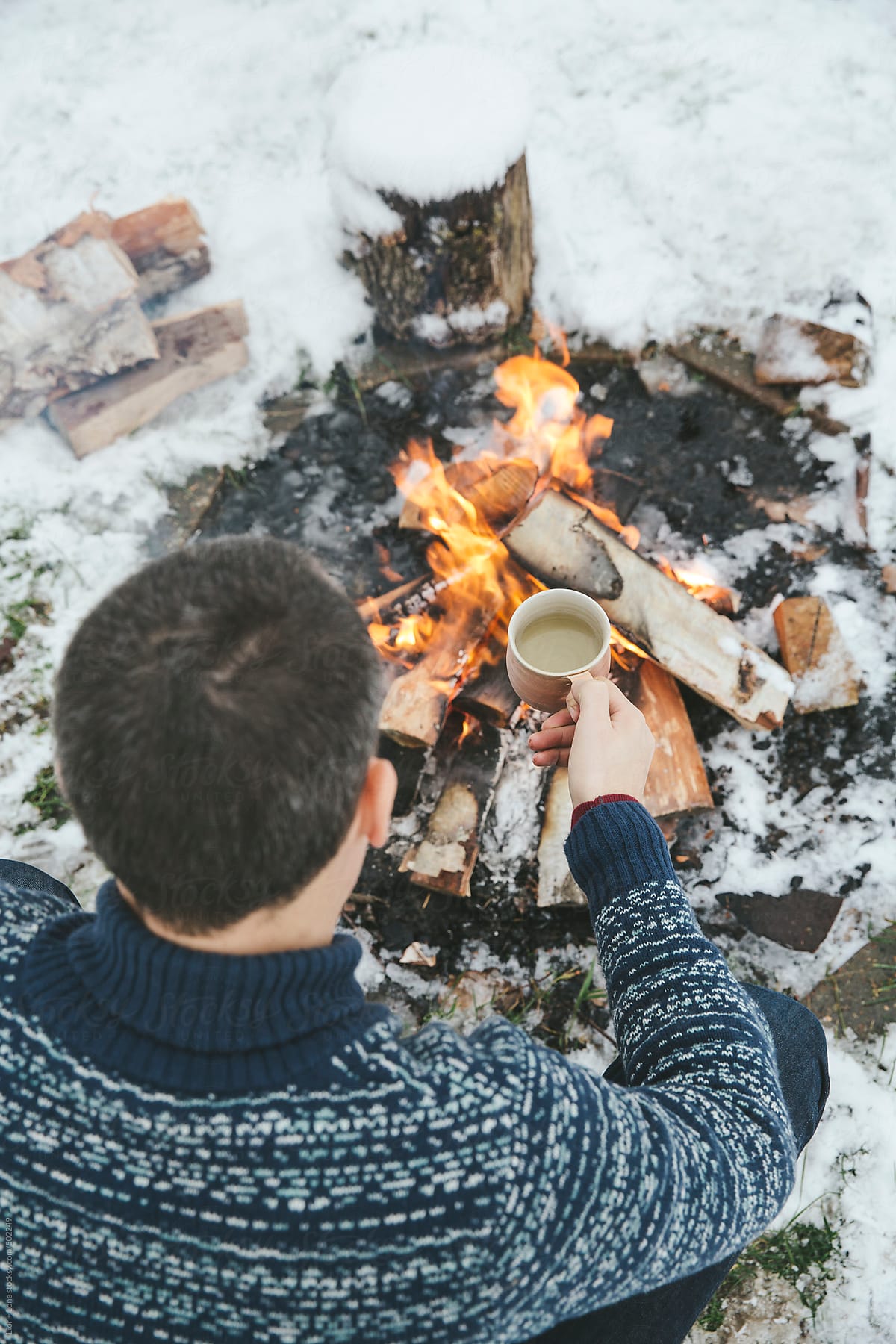Man on a tea break next to bonfire in the snow