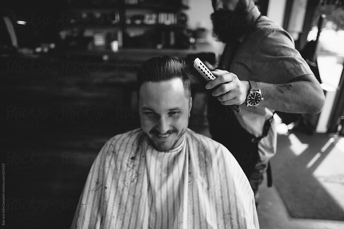 Stylish modern barber giving man a classic haircut - finishing touches