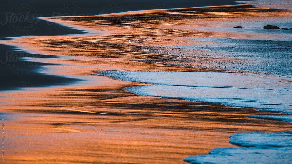 waves creating beautiful abstract patterns in the sand at sunset
