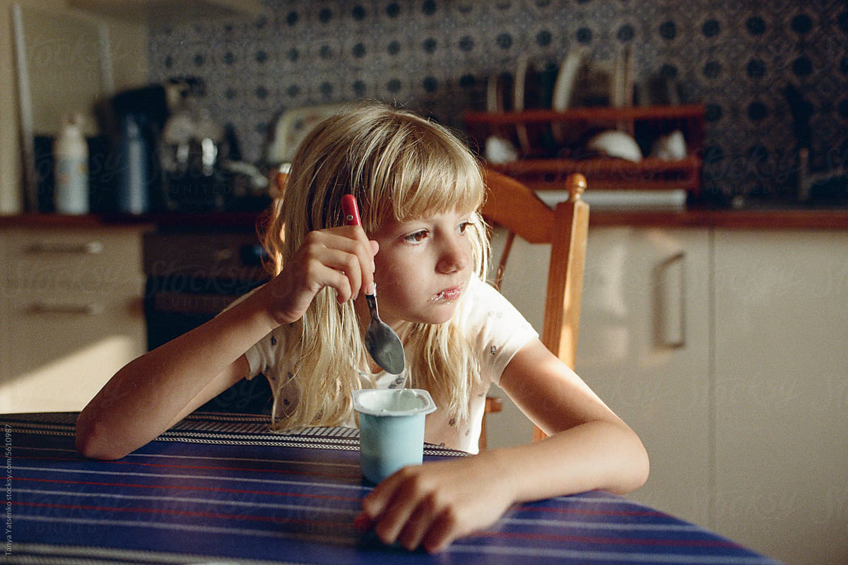 A girl eating a yogurt in the kitchen