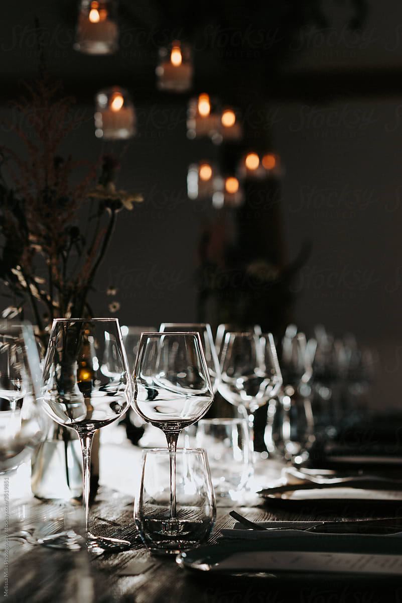 Glasses backlit on a table by night with candles hanging above the table