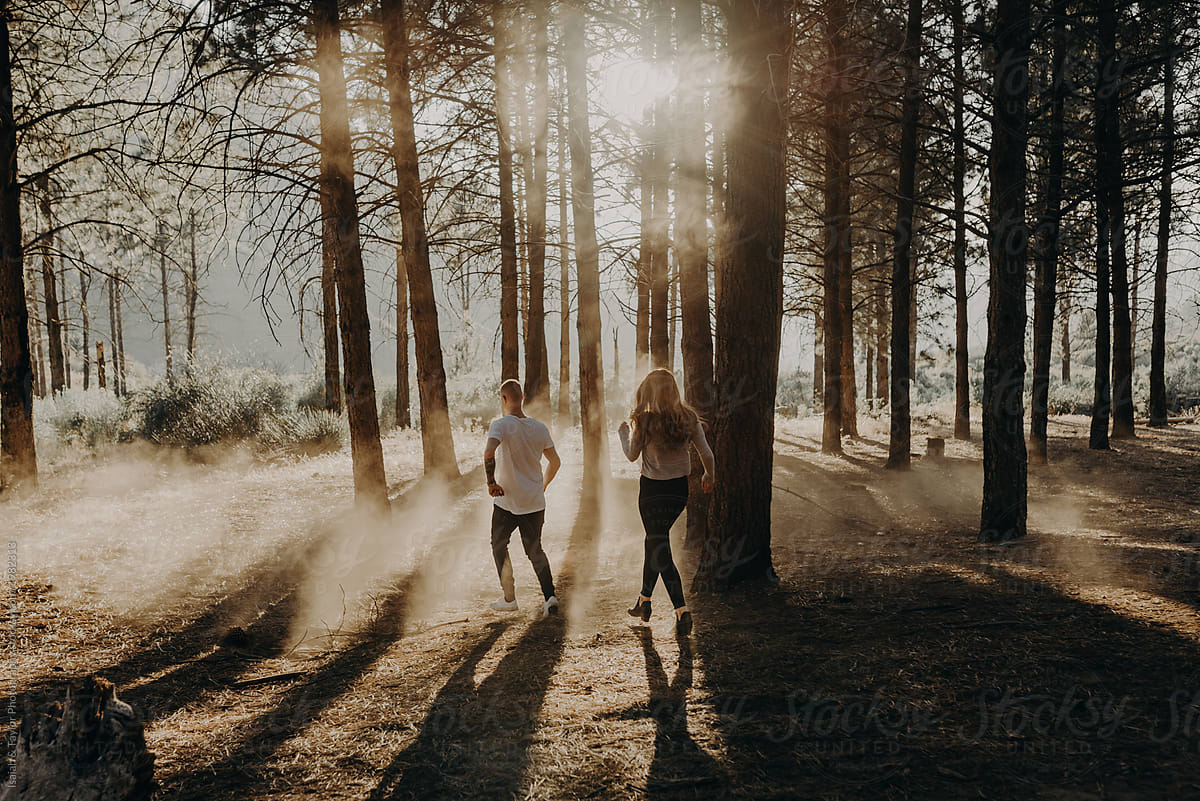 Two people running away into the forest with dreamy sunset light and dust