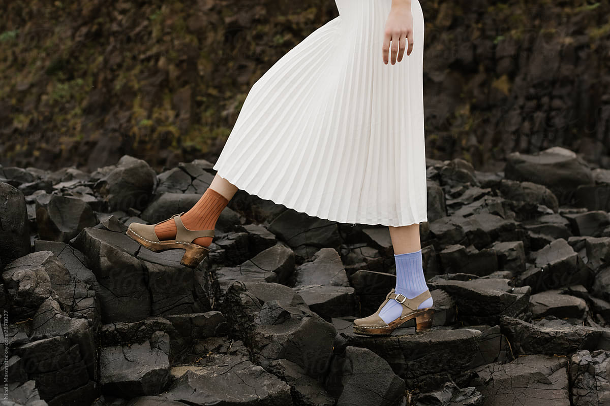 person walking on rocks with long white skirt and different colored socks