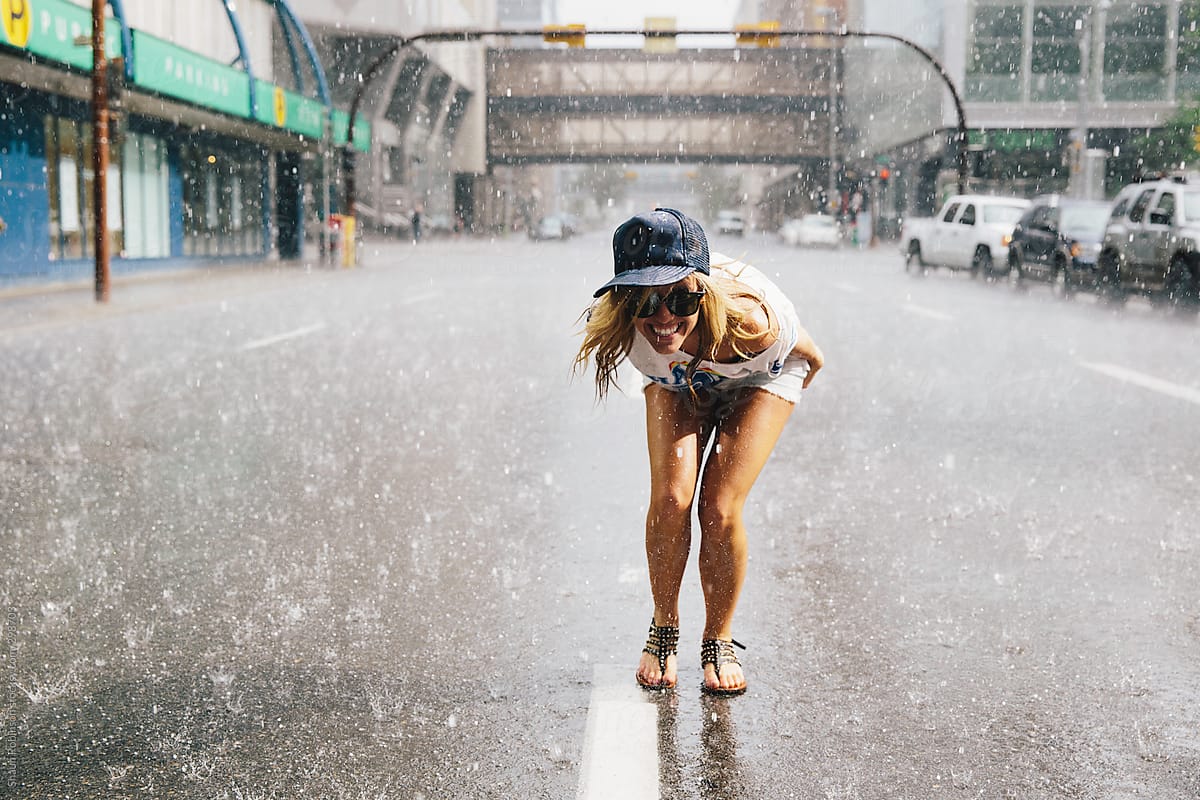 Happy young woman standing in the street in rain