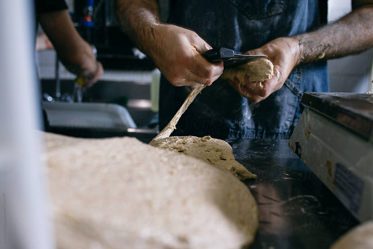 Professional baker with knife working with dough