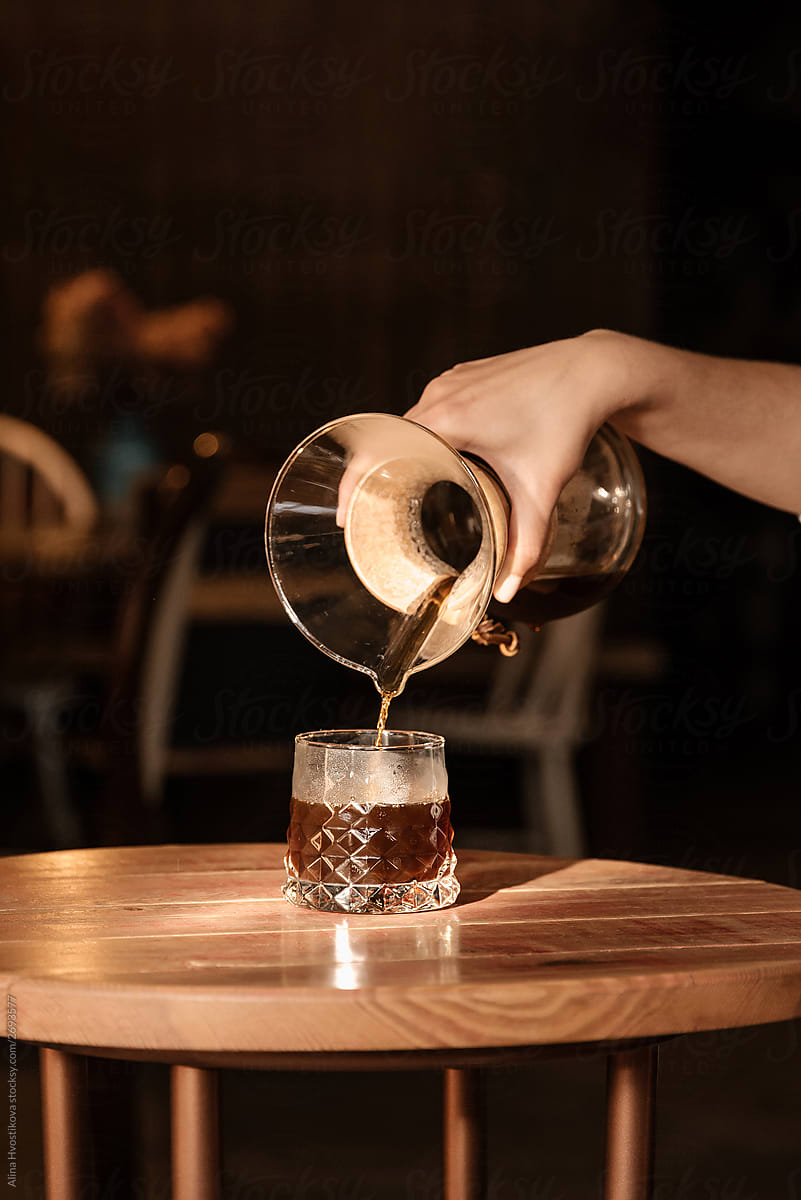 Close up of barista pouring black coffee in glass.