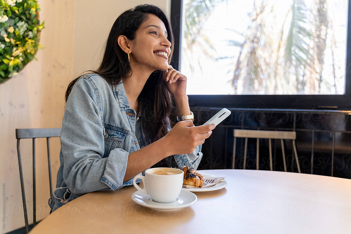 Happy young woman looking at phone in cafeteria