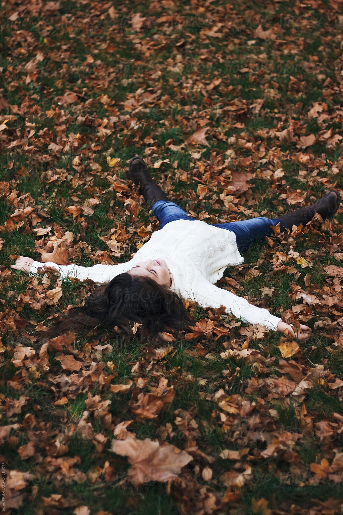 Little girl lie down in autumn leaves in the park