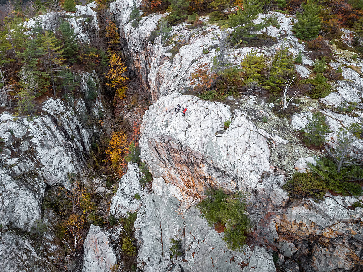 Man Sitting on Top of Mountain Cliff with Autumn Forest