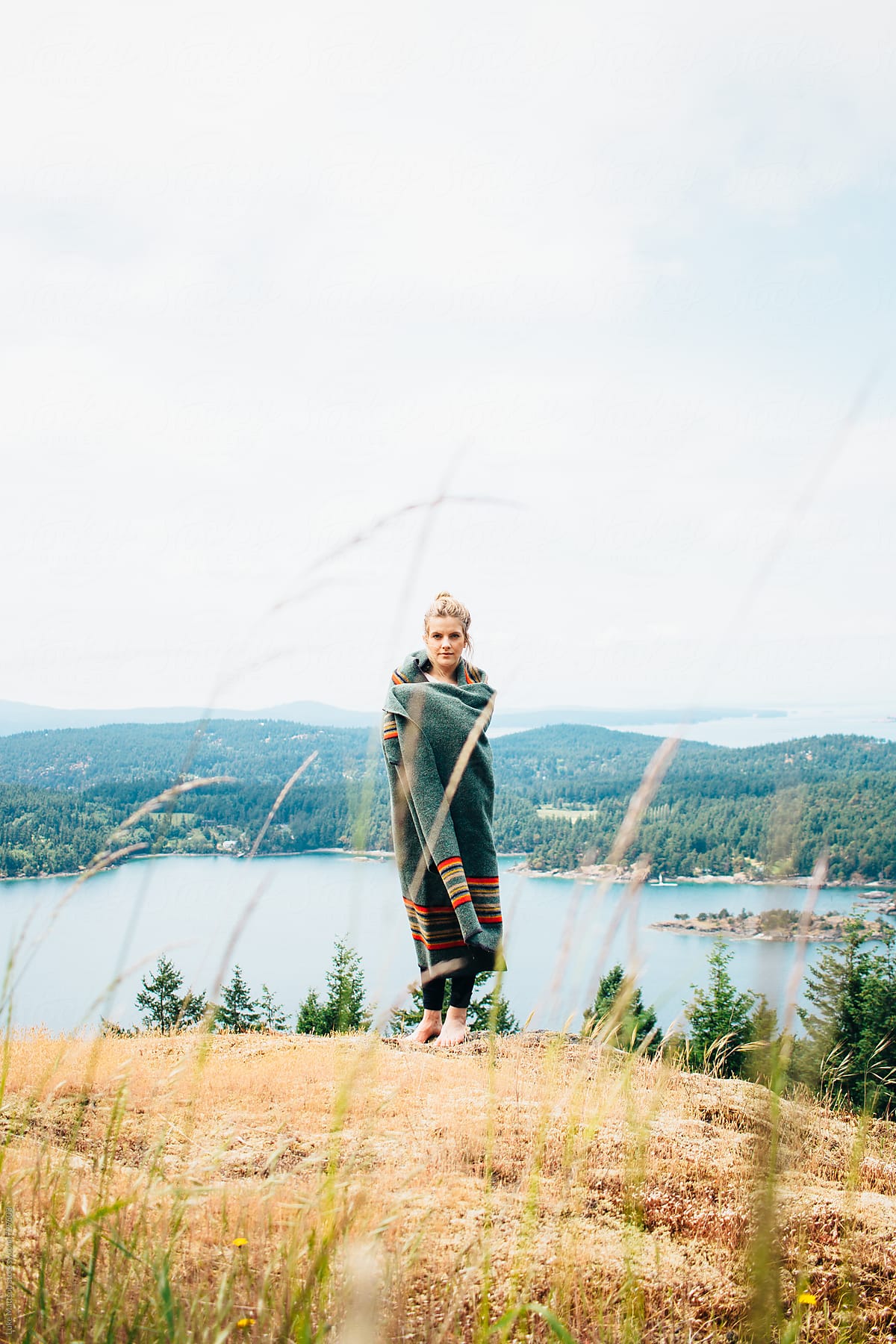 Young Blonde Woman Wrapped In Wool Blanket Standing On Forest Island Hillside By Stocksy