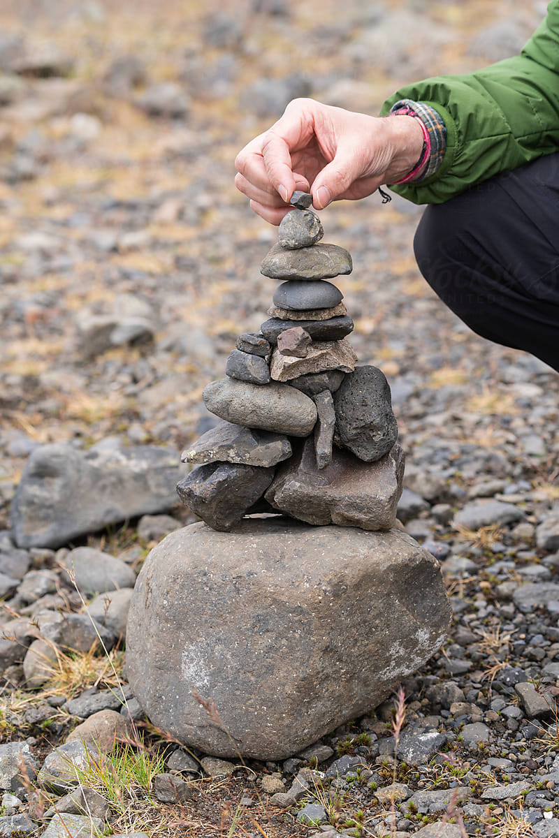 A Man\'s Hand Places A Rock On The Top Of A Stack Of Stones
