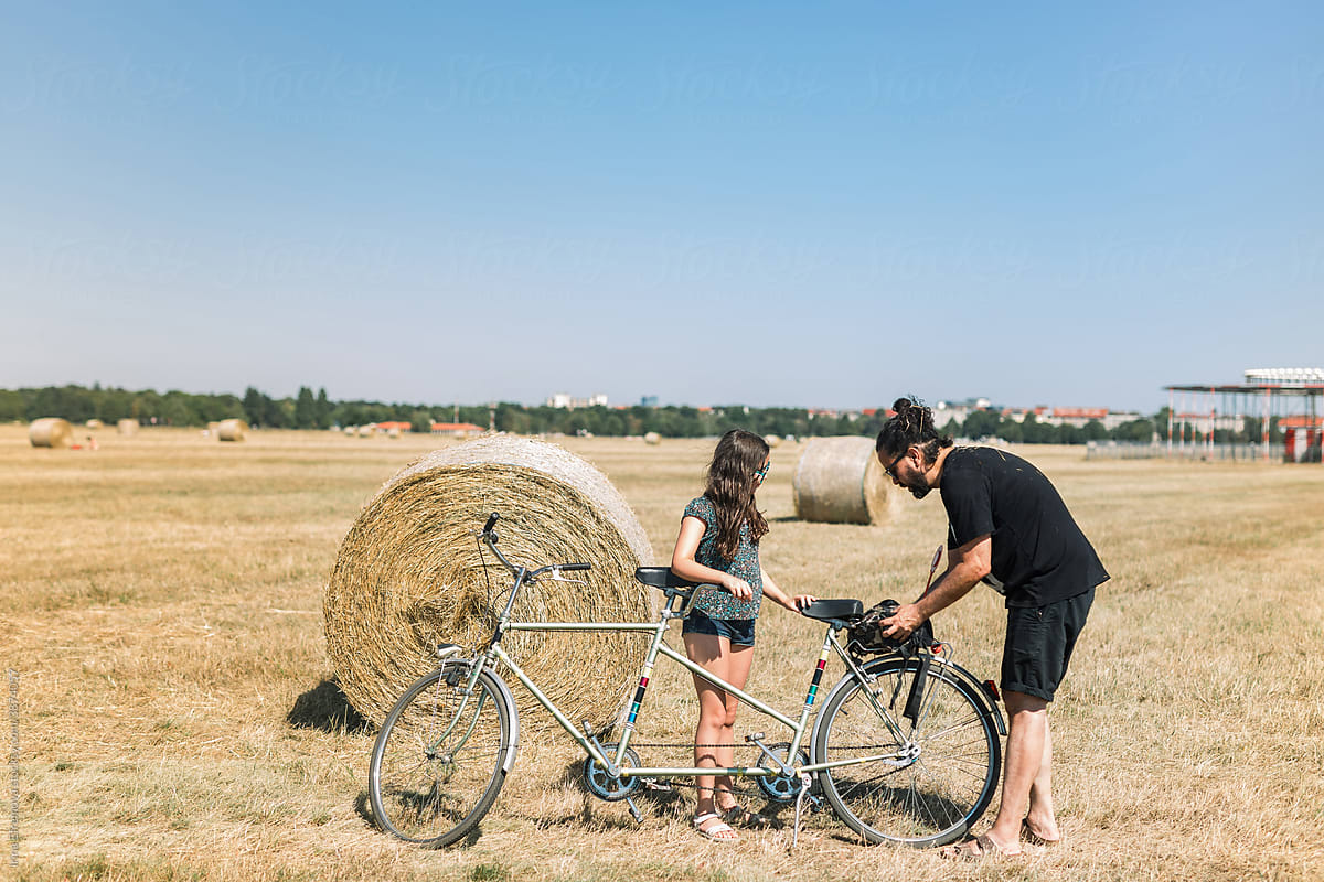 Father and daughter park a tandem bike on the field