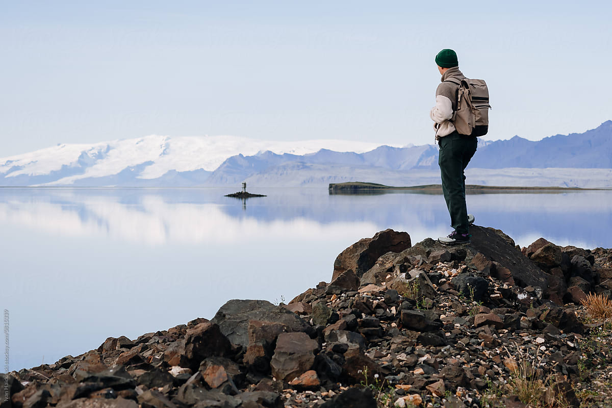 man on stone at glacier lake shoreline. Water reflection