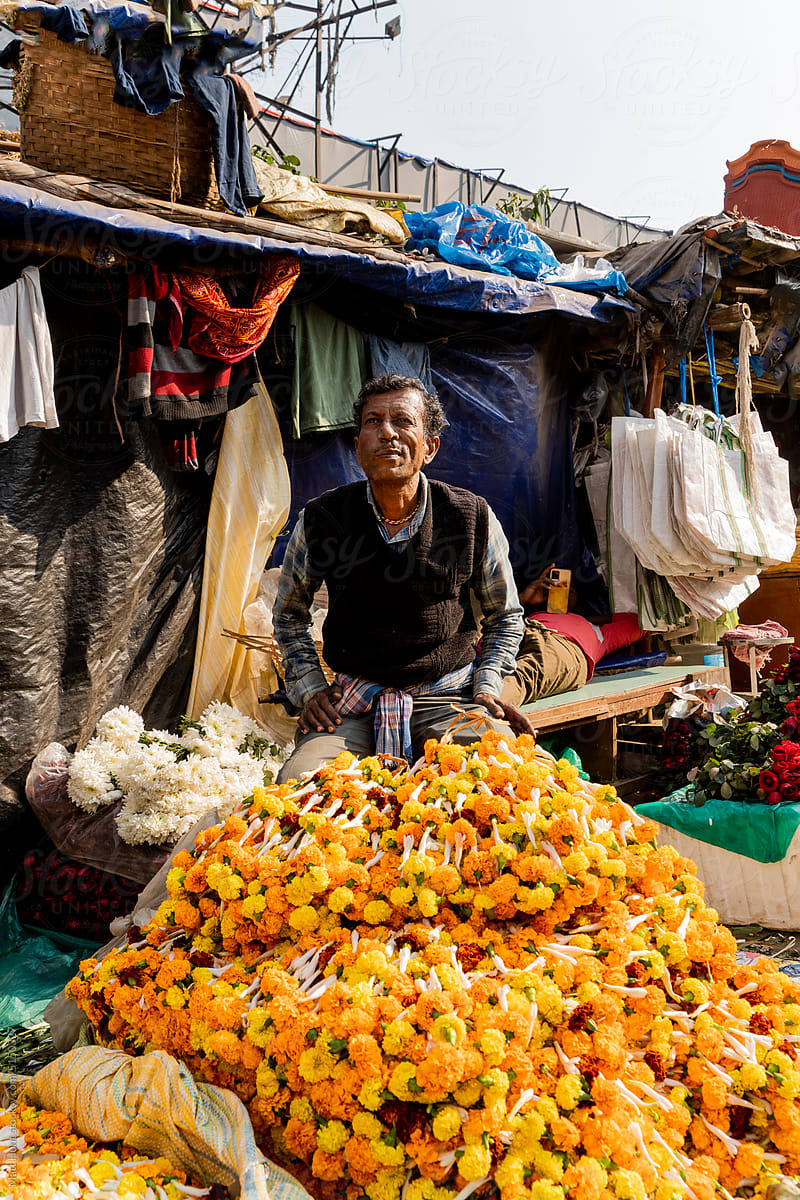 A flower seller poses for a portrait in front of marigolds
