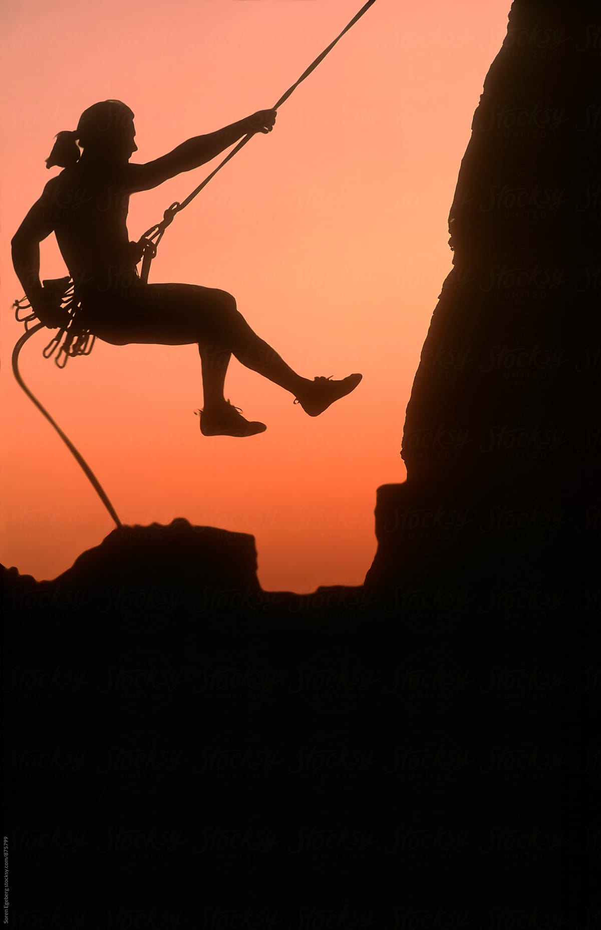 Silhouette of climber rapelling down a cliff face at sunset