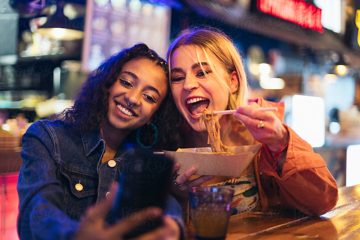Young women in a date taking selfies while eating street food