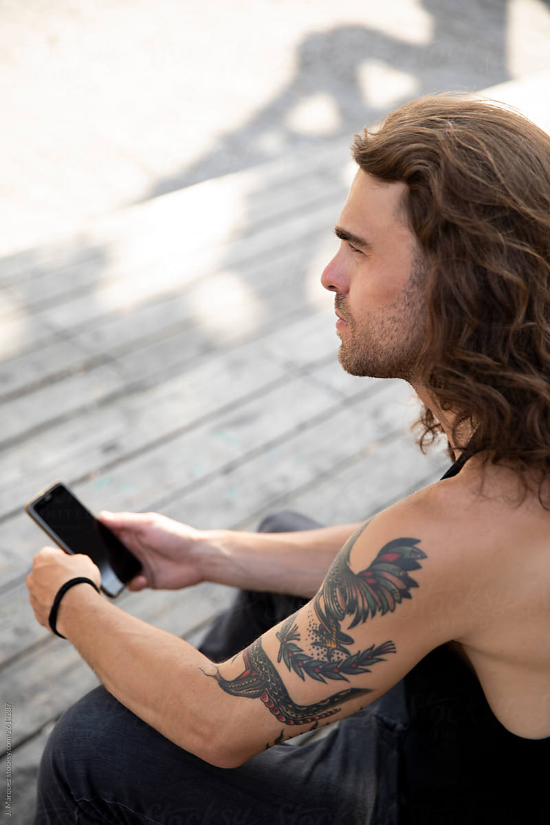 Man with smartphone sitting near wooden wall