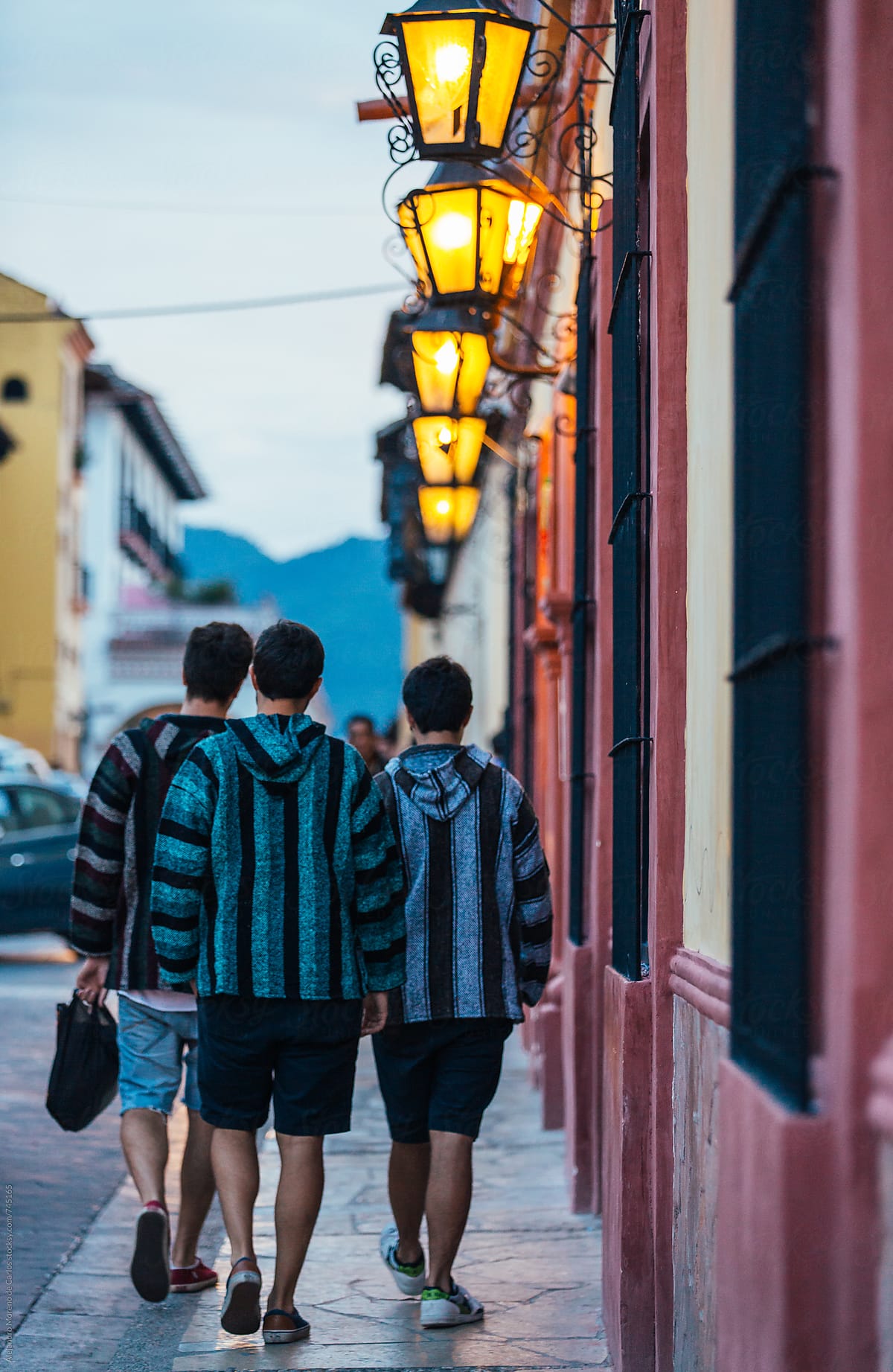 Group of three friends walking down the street of a colonial Mexican city at dusk with poncho sweaters
