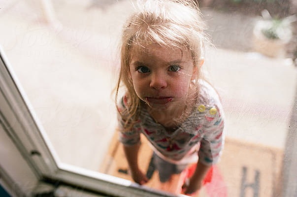 Little Girl Looks Through Front Door Screen by Stocksy