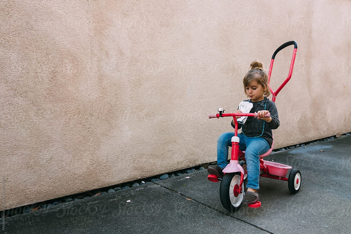 Little girl riding a tricycle and drinking a juice box