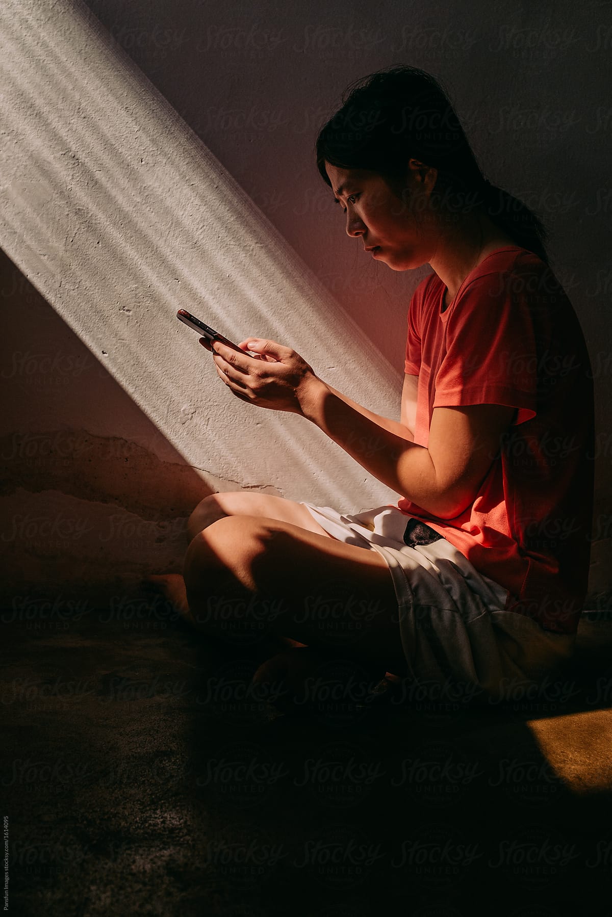 Asian woman using cell phone in dramatic sunlight