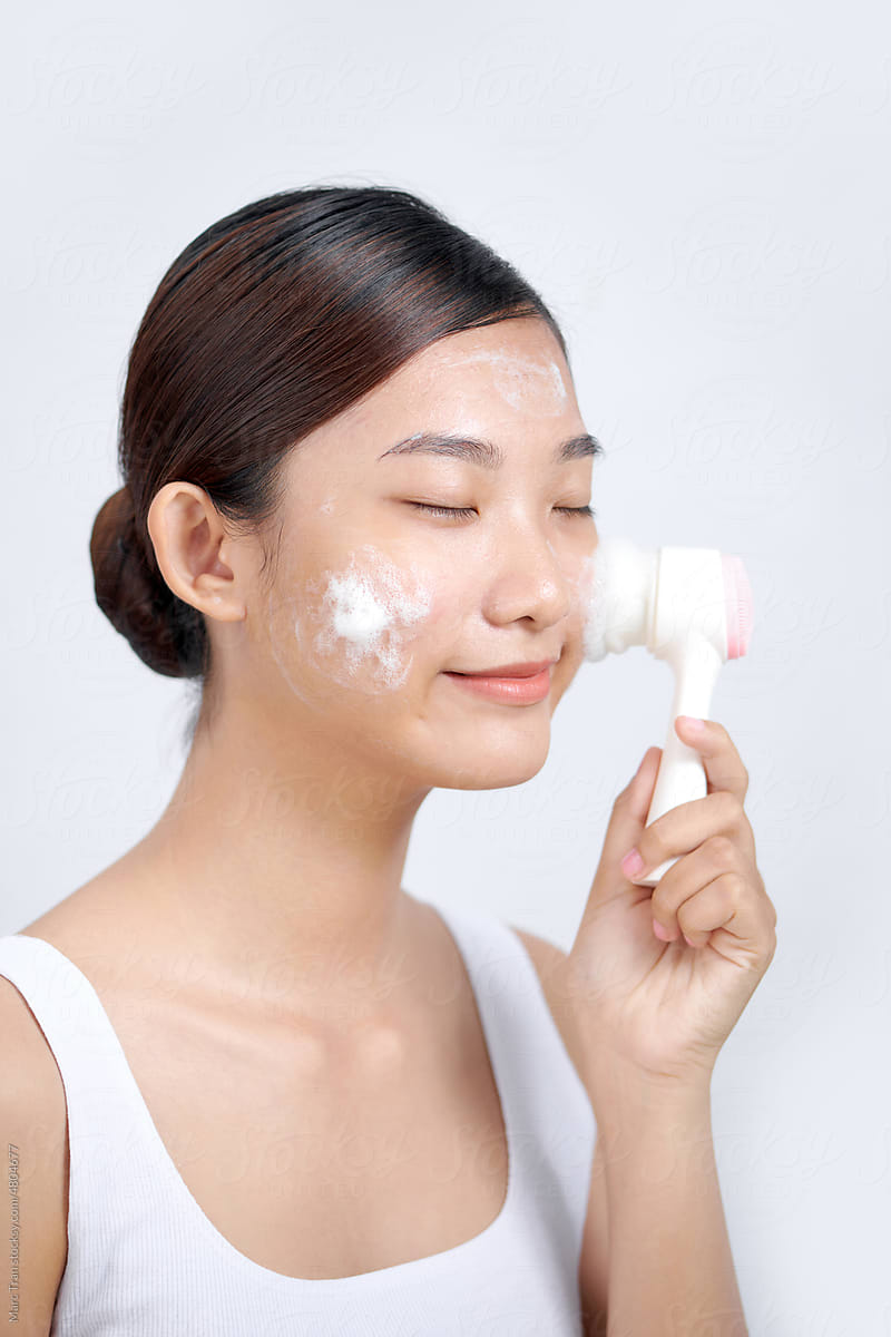 Beautiful woman is washing face skin with brush.