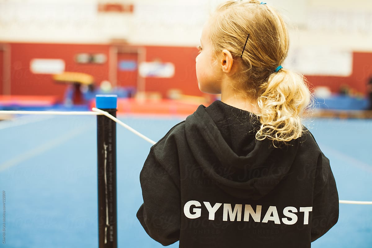 A little gymnast stands at a competition.
