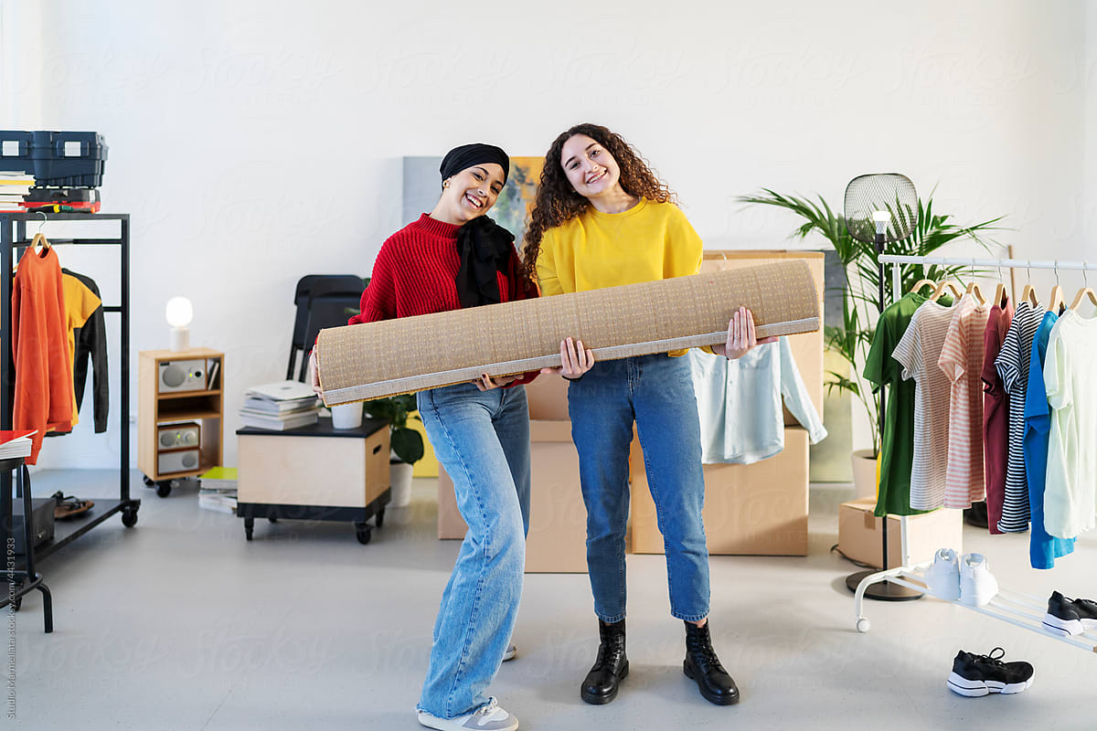 Smiling diverse women with rolled rug in new apartment