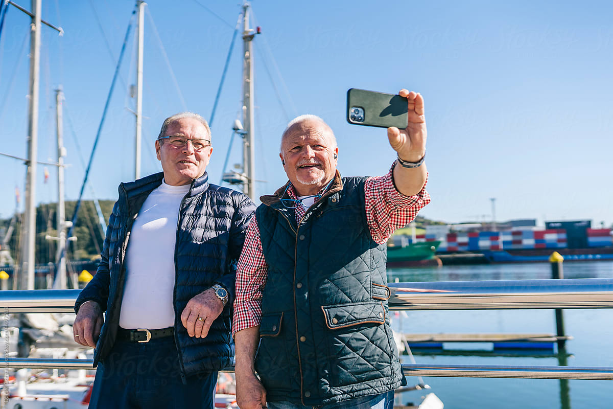 Cheerful retired male friends taking selfie near yachts