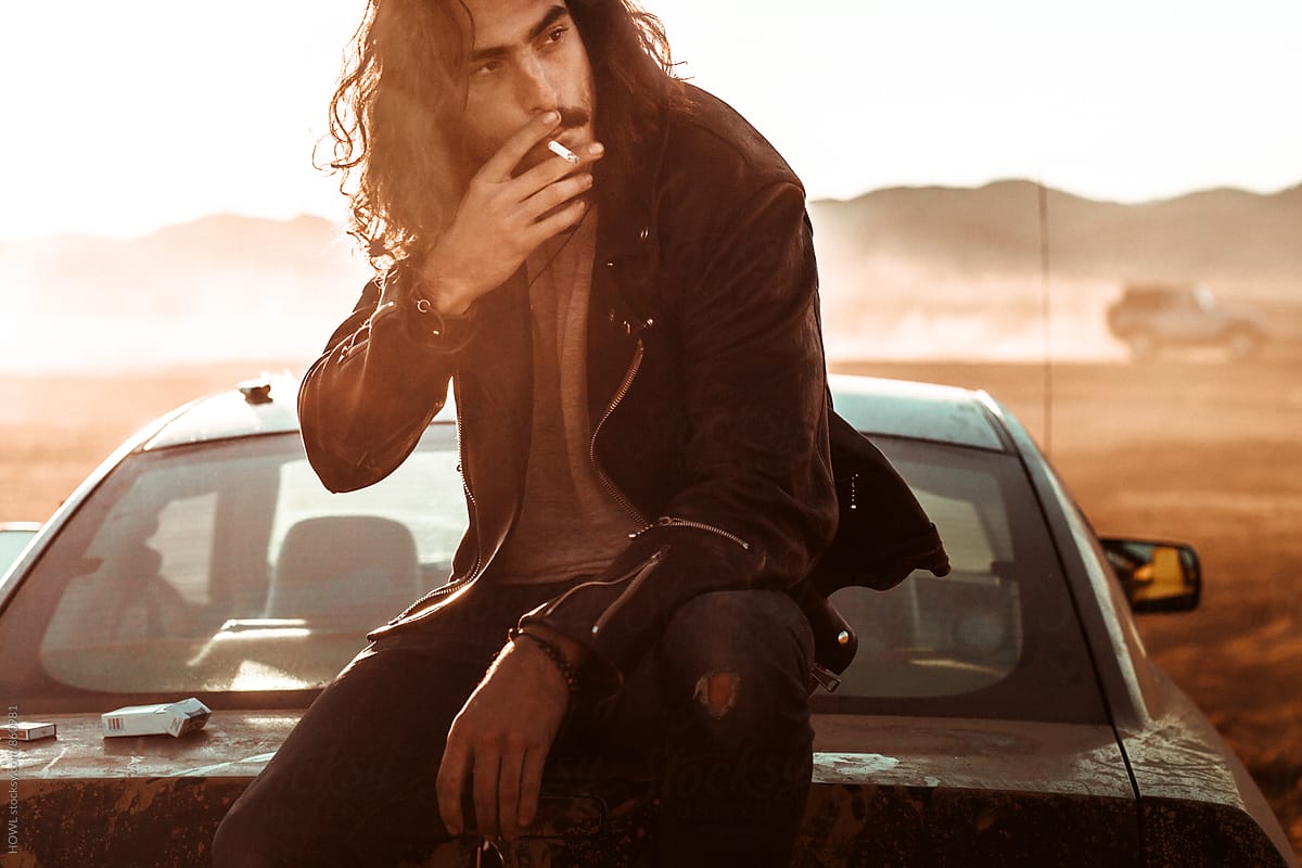 Young hip man smokes a cigarette in the desert