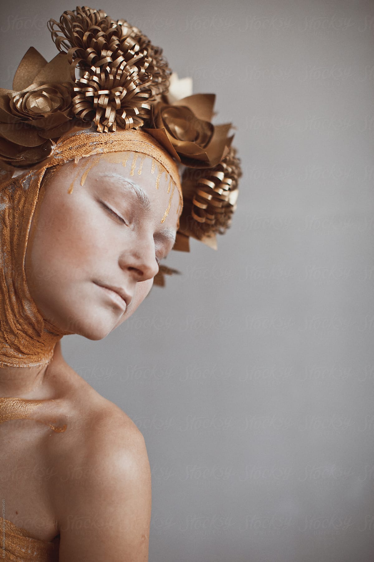 Profile portrait of female with hat of golden paper flowers, weird make up and closed eyes