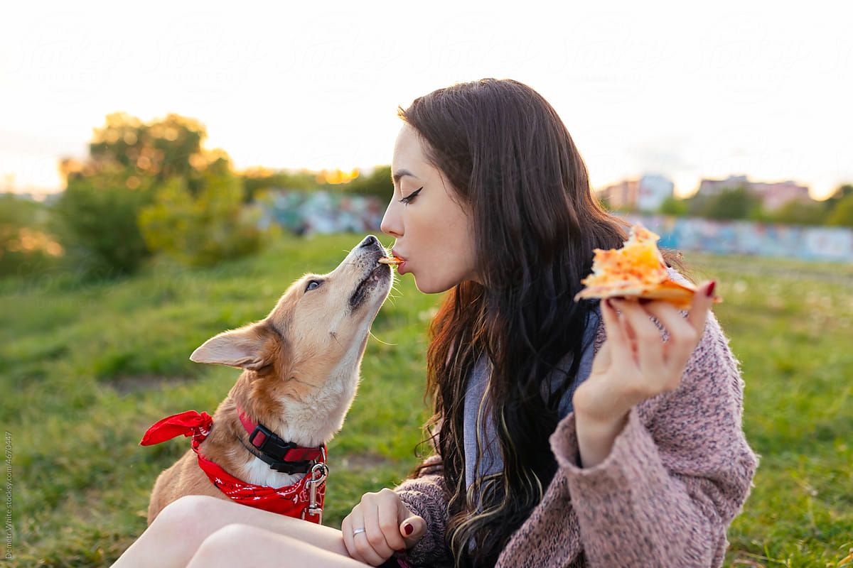 beautiful woman gives a dog a pizza from her mouth