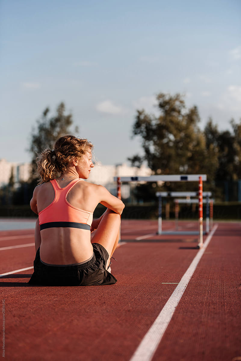 Relaxed female athlete sitting on race track after training