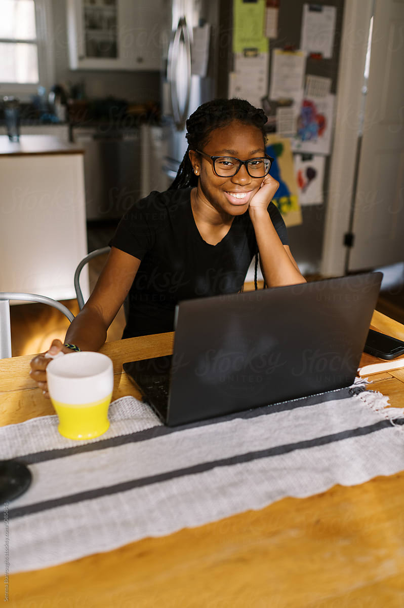 smiling black teenage girl working at her laptop in her home