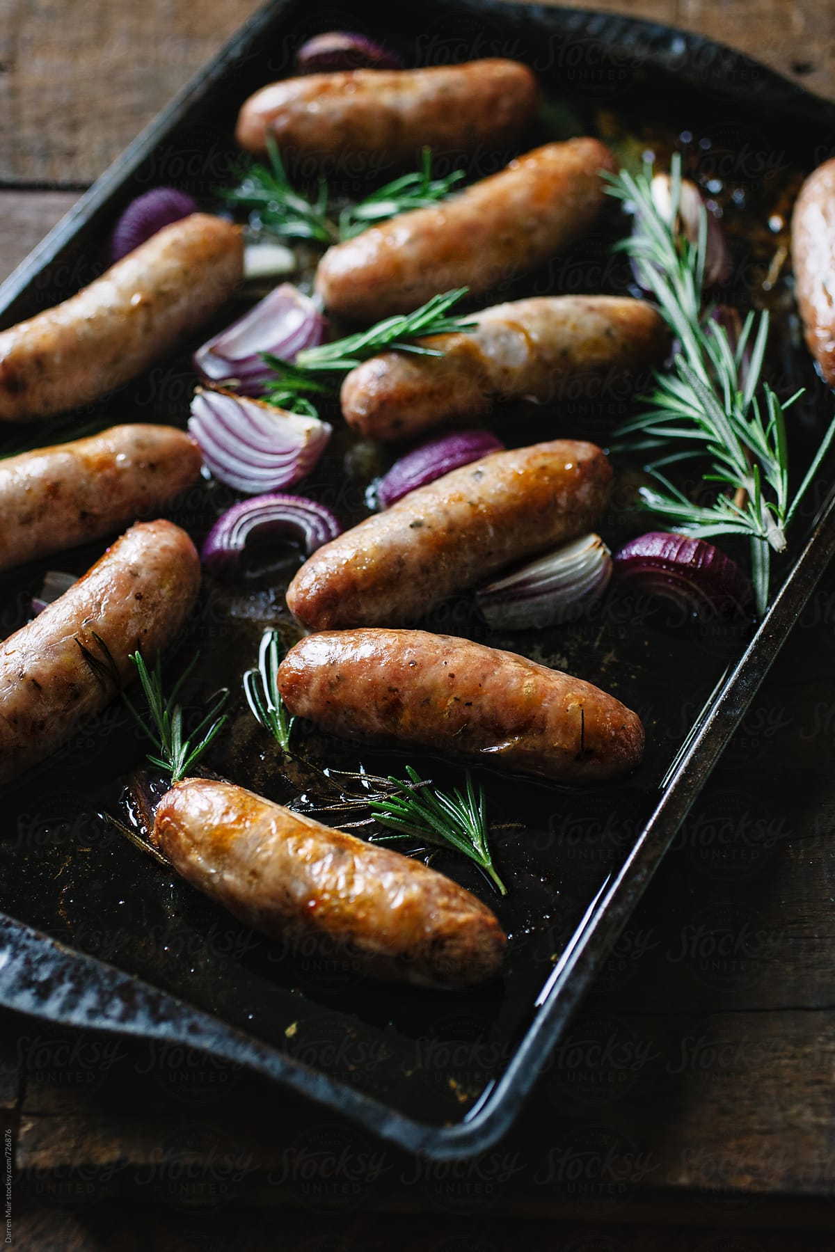 Cooked sausages with red onion and rosemary on a roasting tray.