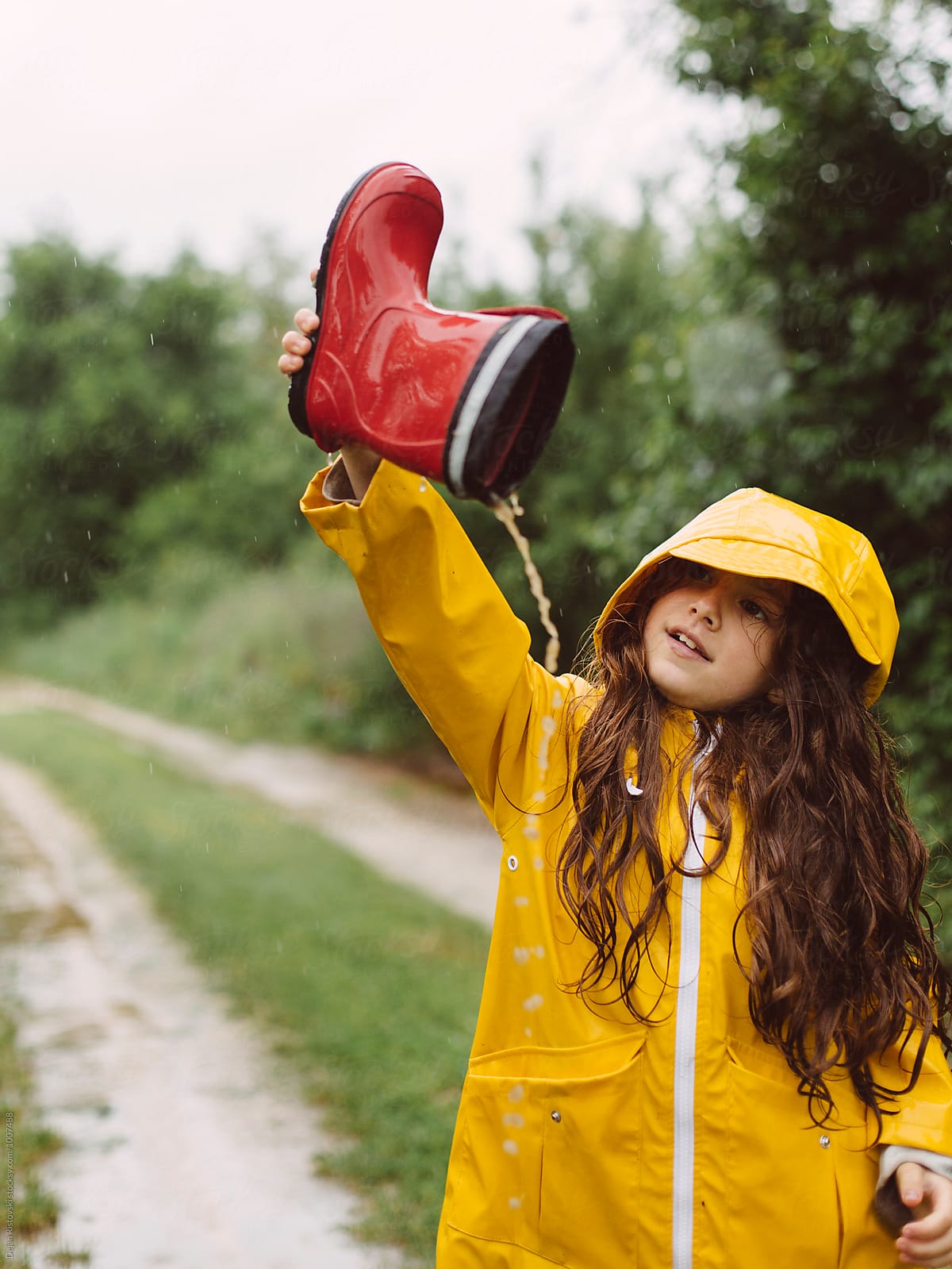 Playful girl pouring rain water from boots.