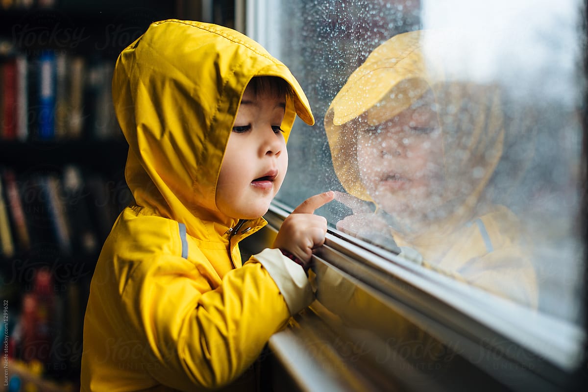 Little kid looking at raindrops on window