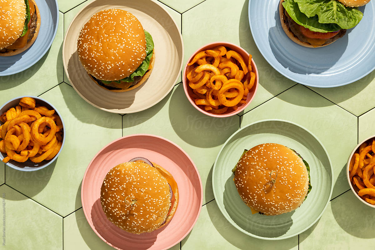 Burgers in colorful plates on green tile background