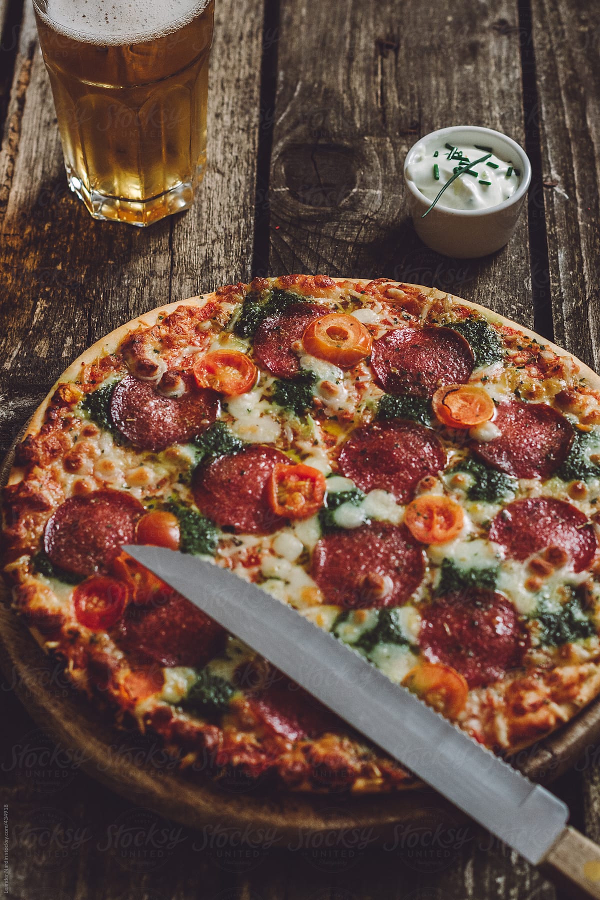 homemade pepperoni pizza with pesto, sour cream dip and a glass of beer on wooden background