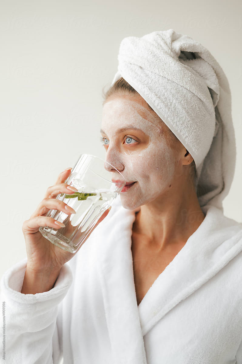 Content lady with facial mask drinking water after bath