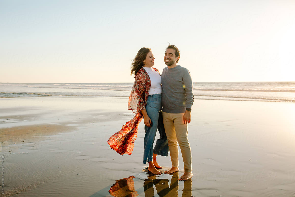 Happy couple standing on shore at sunset