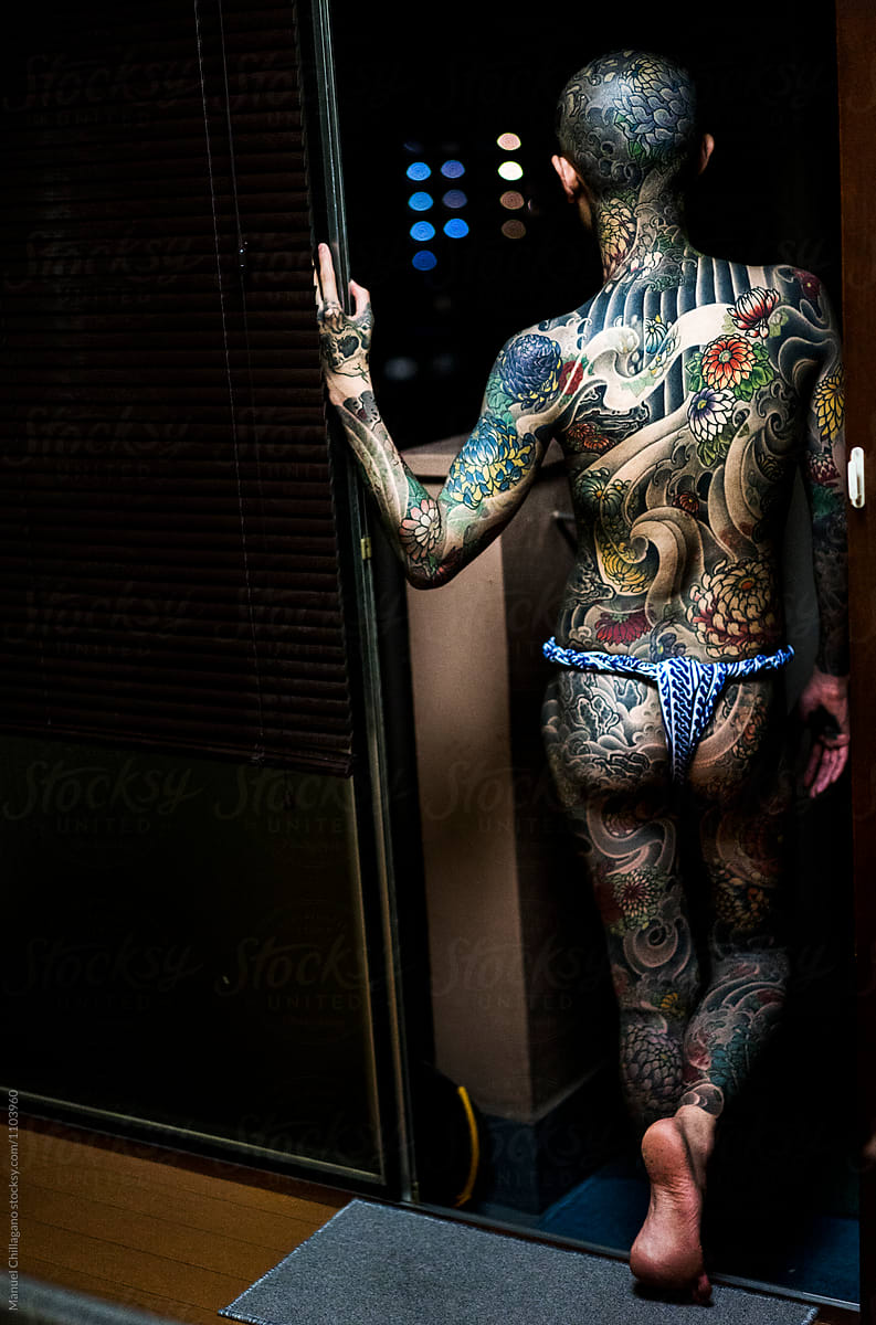 Young man covered in Japanese tattoos looking down from the balcony