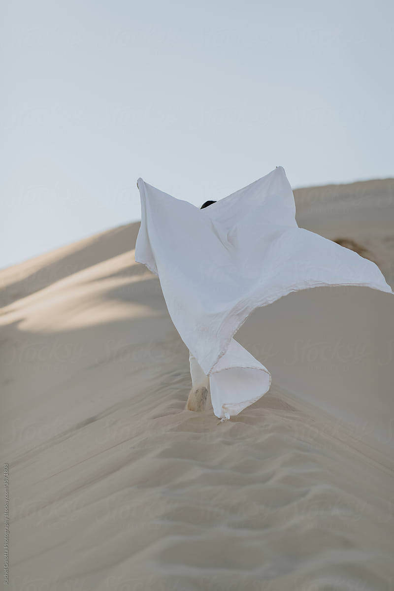 Person Running up a White Desert Sand Dune Holding a White Sheet  Against a White Sky