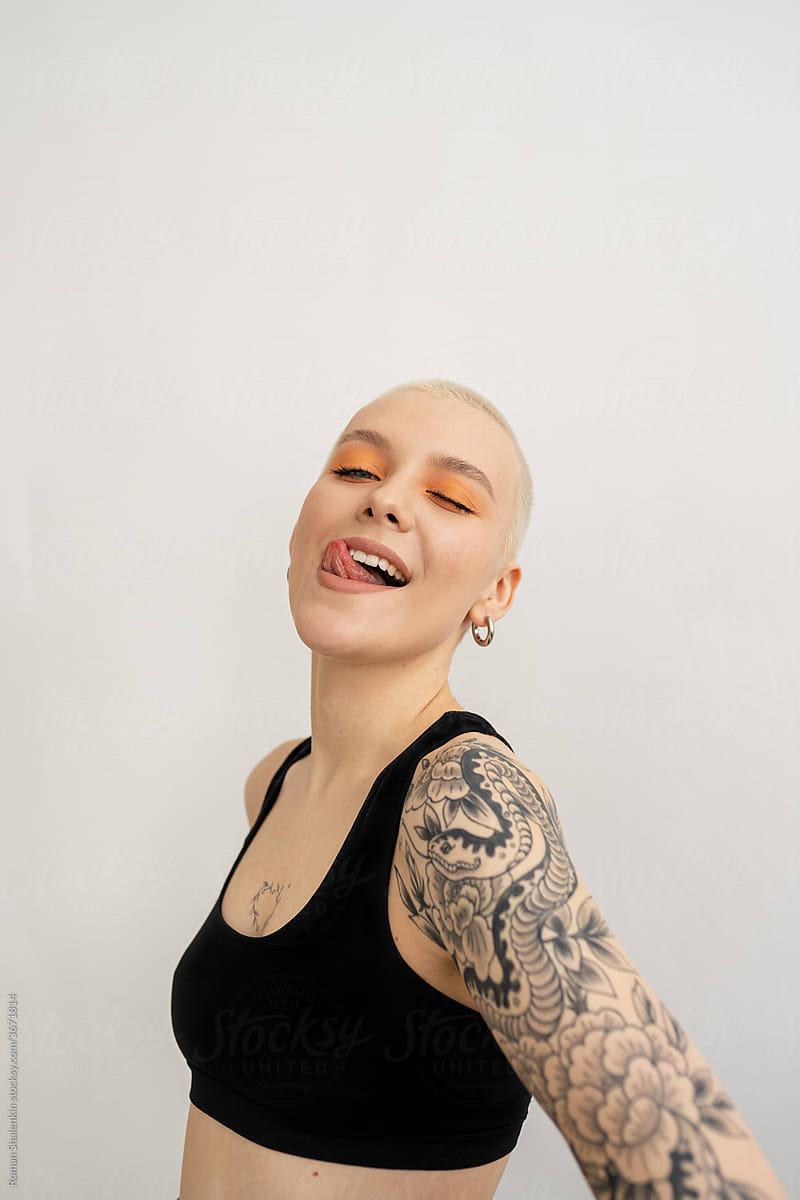 Young woman with short hair and tattoo shows tongue