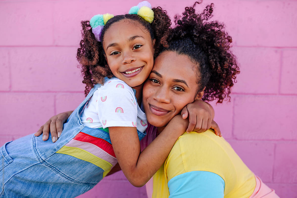 Mother and daughter hugging by pink wall