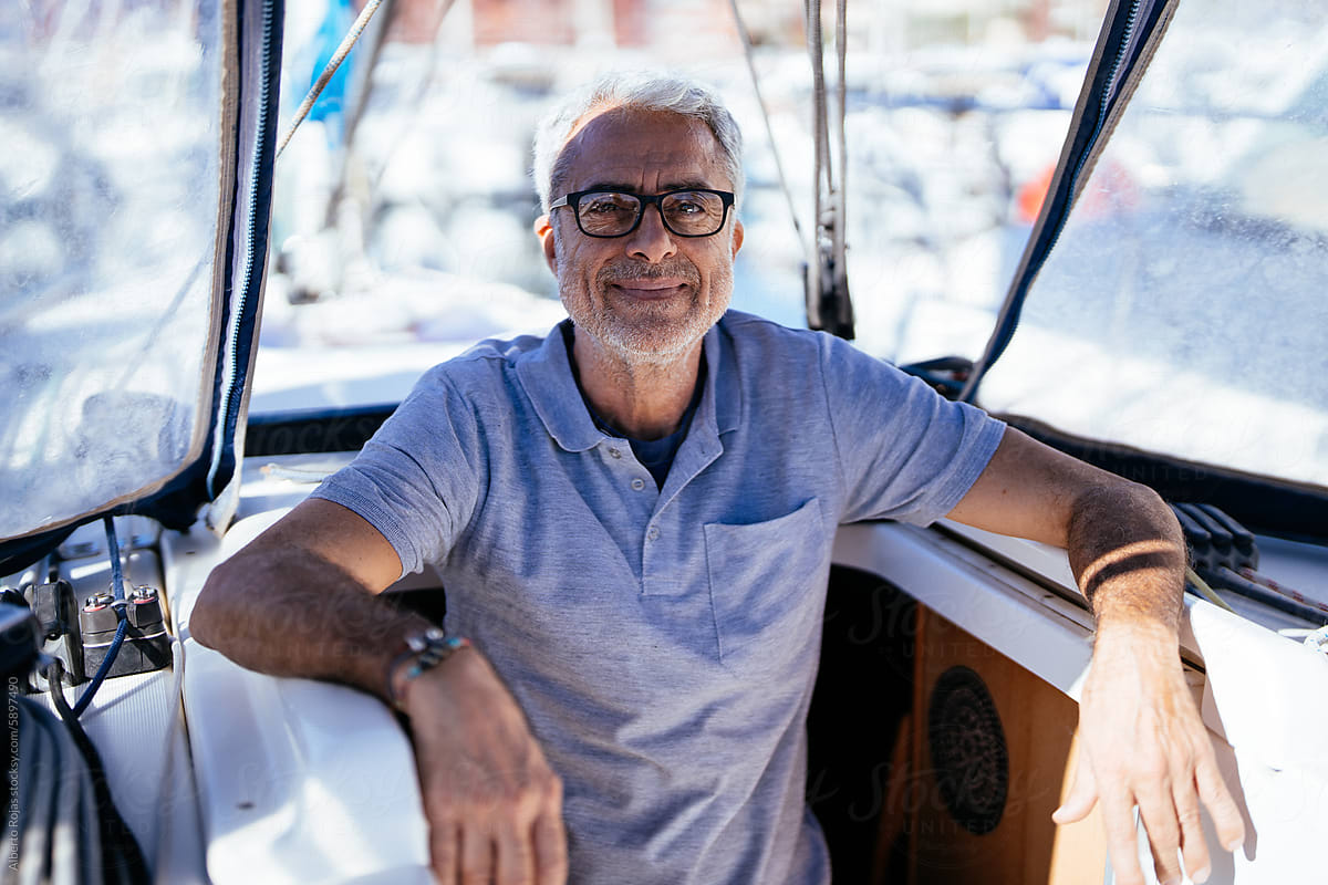 Positive senior man sitting in yacht by glass windshield on sunny day