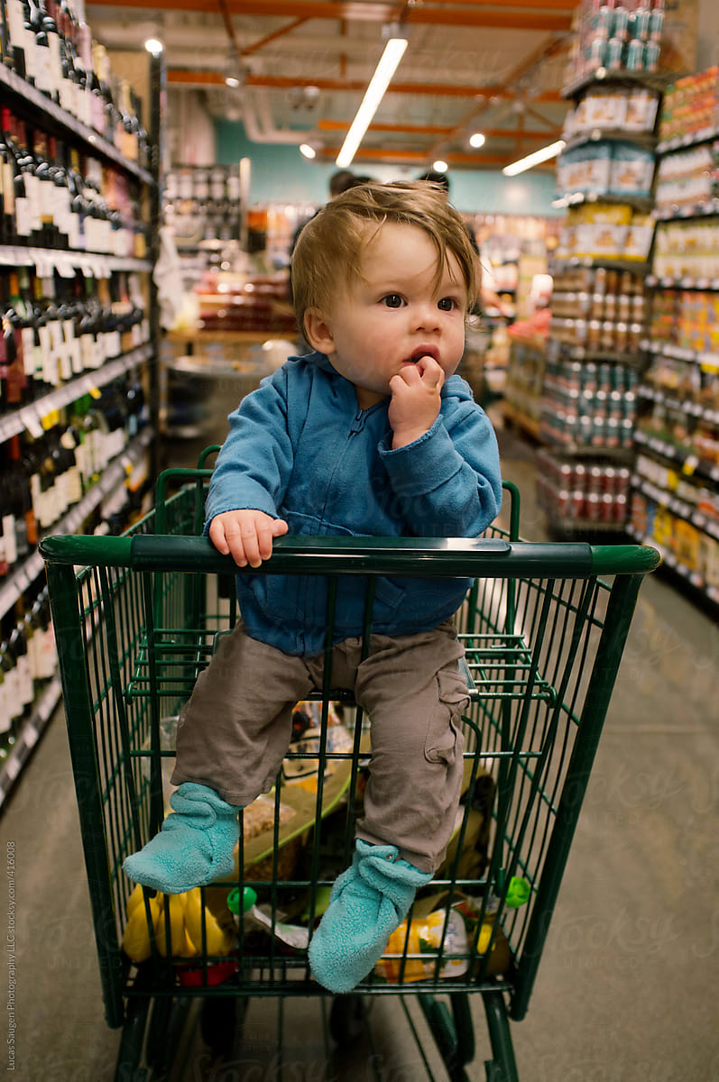 Young baby sitting in a shopping cart at a grocery store.