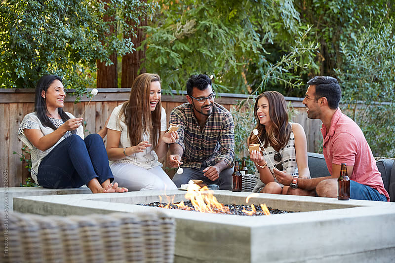 Group of multiethnic millennial friends enjoying drinks by a fire pit in the backyard at home