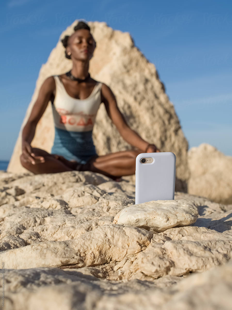 Smartphone near woman meditating on rock
